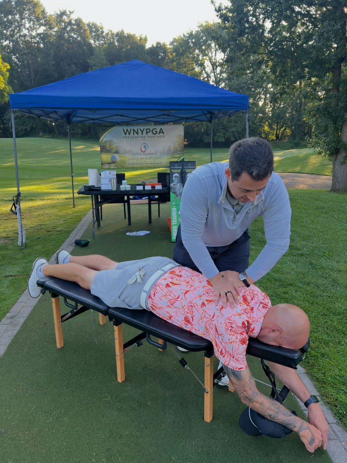Dr. Sam Camarata adjusting a golfer on course under the Camarata Chiropractic WNYPGA Presenting Partner tent